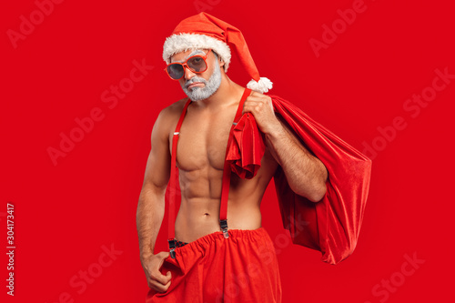 Adult sexy Santa Claus holding sack full of presents, making sad face