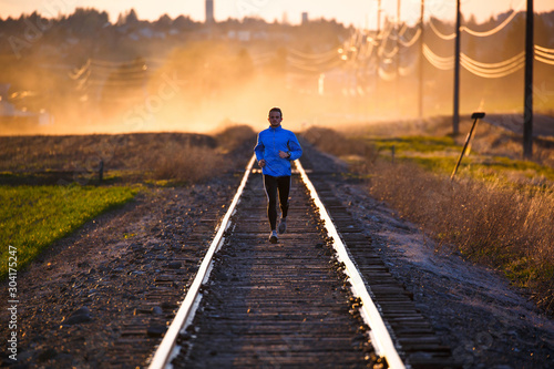 A man on an evening run along abandoned railroad tracks near Pullman, Washington at sunset. The dust cloud is from nearby farming activity.