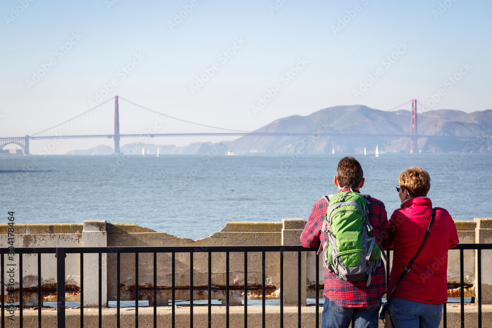San Francisco, California, USA: A tourist couple enjoying the view over the bay with the Golden Gate Bridge from the Aquatic Park Pier. San Francisco, California, USA: A tourist couple enjoying the view over the bay with the Golden Gate Bridge from the Aquatic Park Pier.