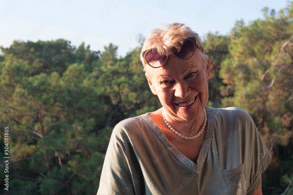 A mature woman in sunglasses on her forehead on the background of a pine forest.