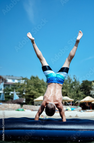 muscular sports boy stands on his hands on an air mattress in the sea against the blue sky all muscles are tense