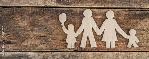 Family with two children, paper figures on wooden background
