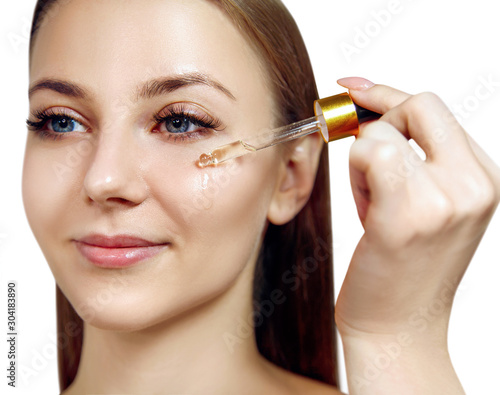 Young woman applying primer oil on face with pipette.
