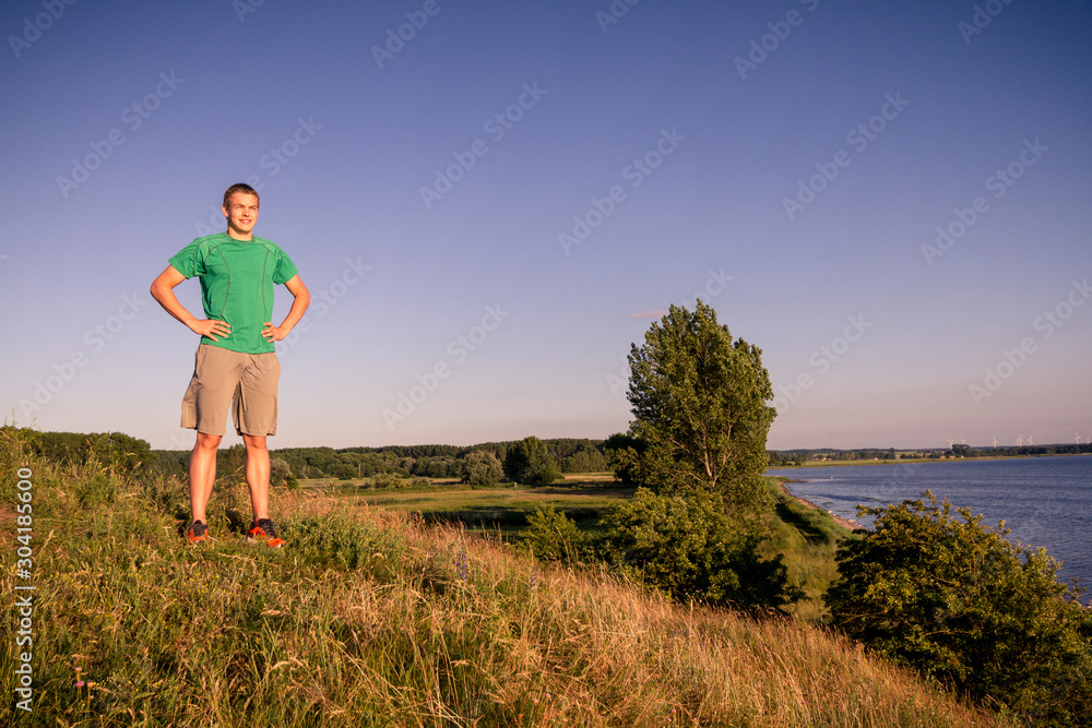 A young sportive man standing on a hill next to the laggon in Rerik after running during sunset.