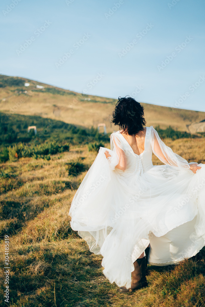 woman in wedding dress is running in the mountains back
