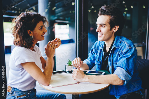 Friendly warm meeting of hipster guys dressed in casual wear in cafeteria.Positive young man with cheerful female blogger discudding funny publication and plan of cooperation in cafe