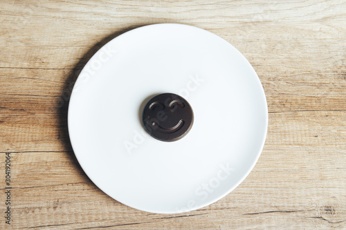 Chocolate cookies with a smiling face, smile, lie on a white plate standing on a wooden table. place for the inscription.