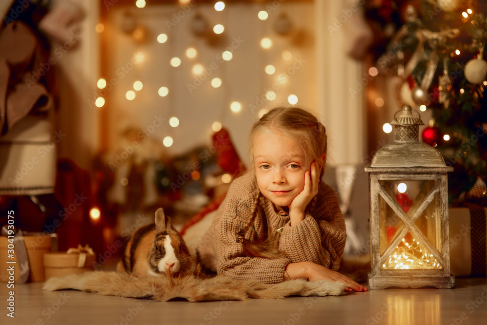 Happy little girl with brown rabbit at Christmas eve - obrazy, fototapety, plakaty 