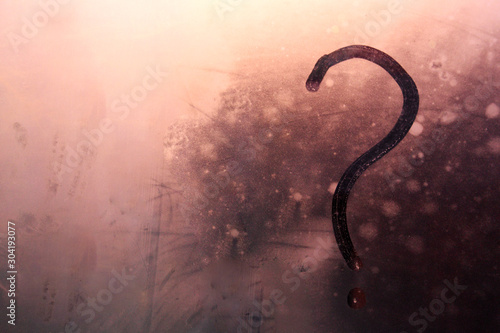 A drawn question mark on a foggy, foggy window. Blurry Question Mark Against Fog Condensation Window Glass Natural Surface Background