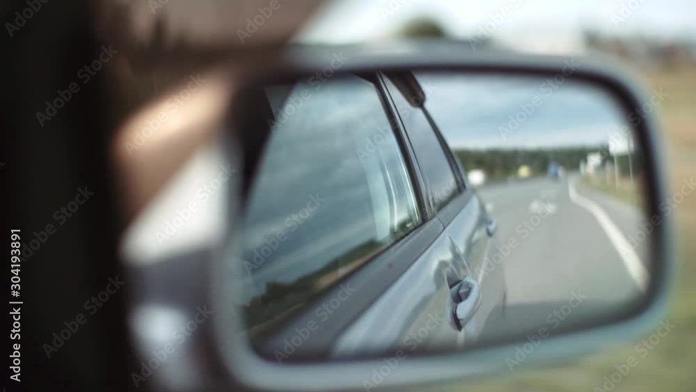 The car goes on the road, side view of the right rear-view mirror, reflection in the glass. View of the right rear-view mirror in motion from the passenger compartment. The car goes on the road, side view of the right rear-view mirror, reflection in the glass. View of the right rear-view mirror in motion from the passenger compartment.