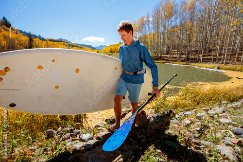 A man carries a SUP board away froma an alpine lake near Telluride, Colorado in autumn in the San Juan Mountains. photo