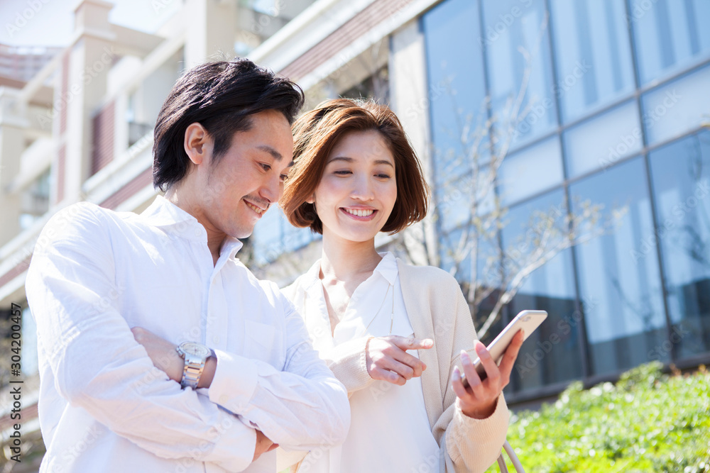 屋外でスマホをチェックする笑顔の男女 屋外でスマホをチェックする笑顔の男女