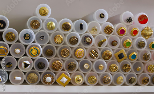 a large number of gold buttons with inserts of different colors in plastic containers on a white background concept of shop or factory of fabrics, handwork, knitting or embroidery