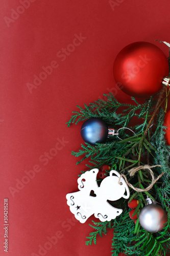 spruce branches with Christmas balls of different colors and a wooden angel on a red background in the corner place for text. concept new year and Christmas