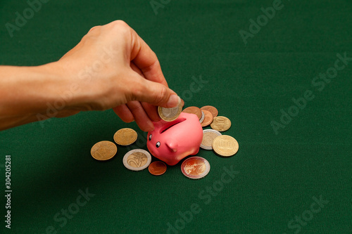 Piggy bank in the form of a pink pig and euro coins and cents on a green background. Invest in the future by raising money. Female hand puts a coin in the piggy bank slot photo