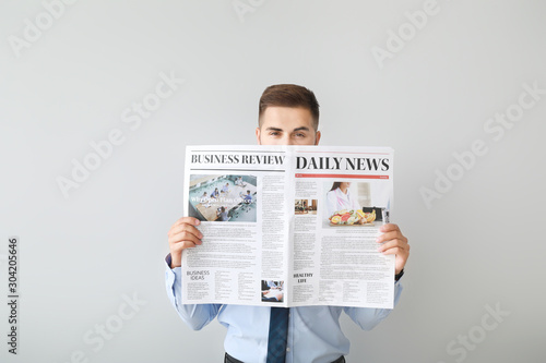 Handsome businessman with newspaper on light background photo