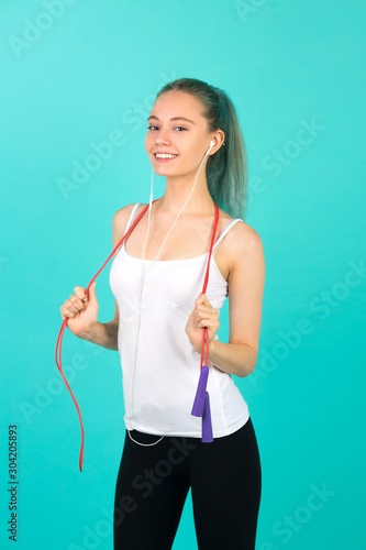 beautiful young slim woman in sportswear on a blue background with a skipping rope in hands