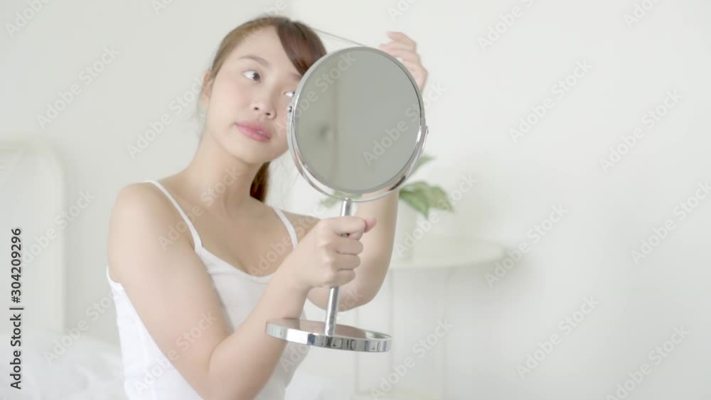 Beauty portrait young asian woman smiling look at mirror of checking skin care caucasian with wellness in the bedroom, beautiful girl happy face for health, lifestyle and wellbeing concept. Beauty portrait young asian woman smiling look at mirror of checking skin care caucasian with wellness in the bedroom, beautiful girl happy face for health, lifestyle and wellbeing concept.