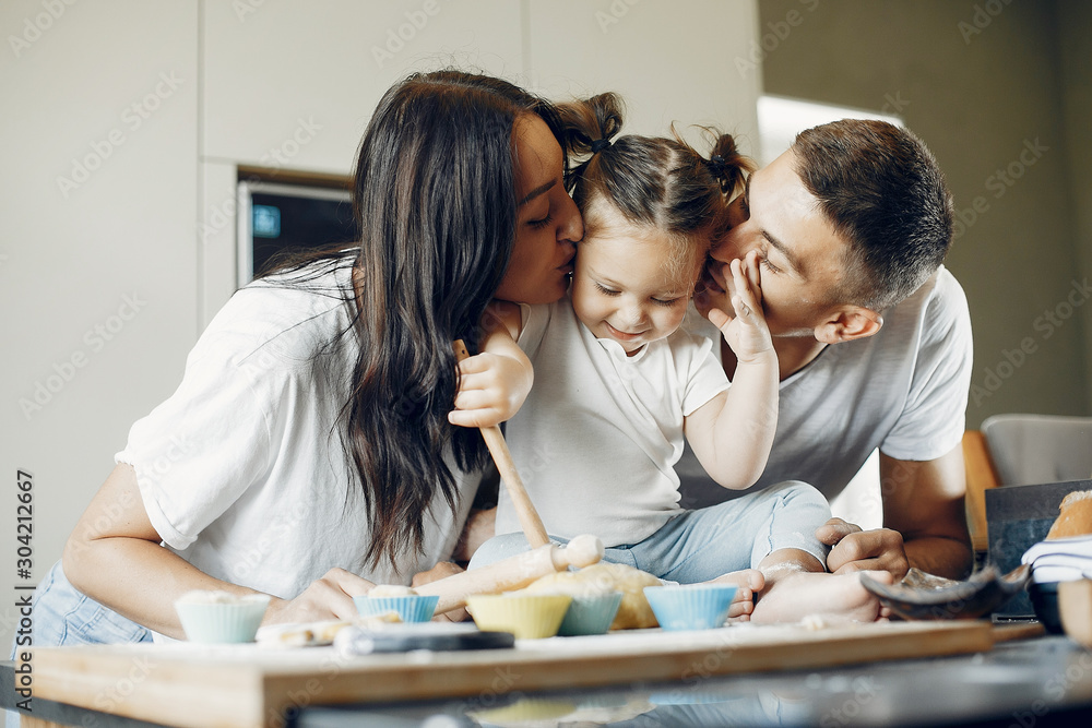 Fototapeta premium Family in a kitchen. Little girl with a dough. Mother and father in a white t-shirts