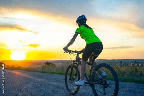 Beautiful girl cyclist rides a bicycle on the road in the sunset. Healthy lifestyle and sport.