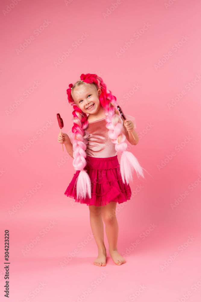 cute little girl in a pink dress with pink braids from kanekalon holds heart-shaped lollipops in her hands