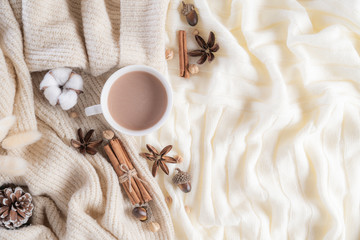 Autumn or winter composition. Coffee cup, cinnamon sticks, anise stars, beige sweater on cream color knitted blanket background. Flat lay top view copy space.