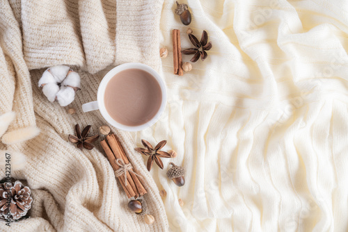 Autumn or winter composition. Coffee cup, cinnamon sticks, anise stars, beige sweater on cream color knitted blanket background. Flat lay top view copy space.