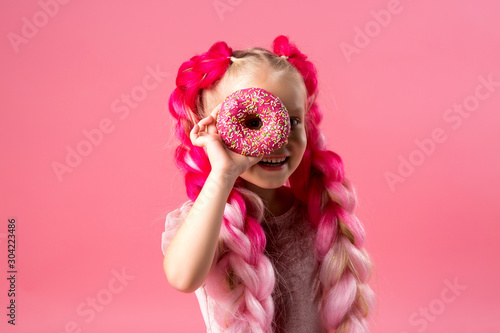 cute little girl in a pink dress with pink braids from kanekalon holds donuts in pink glaze in her hands photo