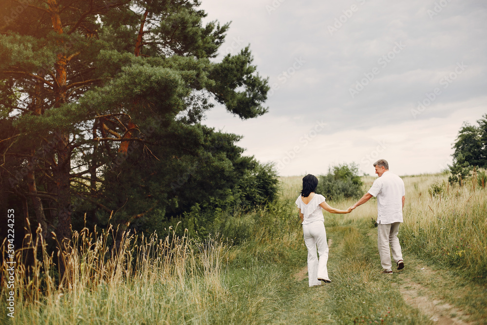 Adult couple in a summer field. Handsome senior in a white shirt. Woman in a white blouse Adult couple in a summer field. Handsome senior in a white shirt. Woman in a white blouse