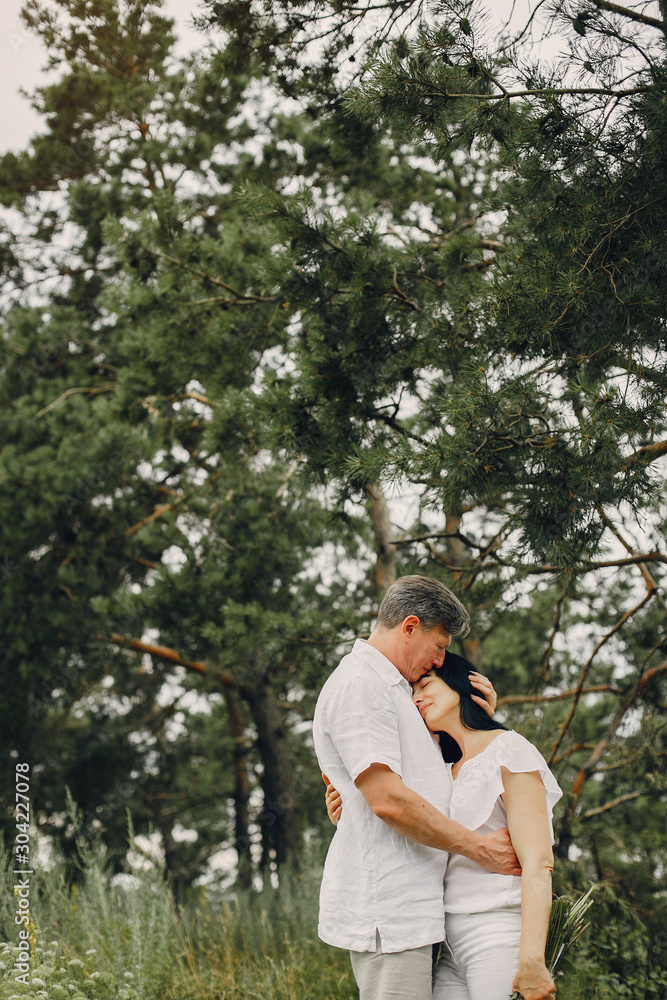 Adult couple in a summer field. Handsome senior in a white shirt. Woman in a white blouse Adult couple in a summer field. Handsome senior in a white shirt. Woman in a white blouse
