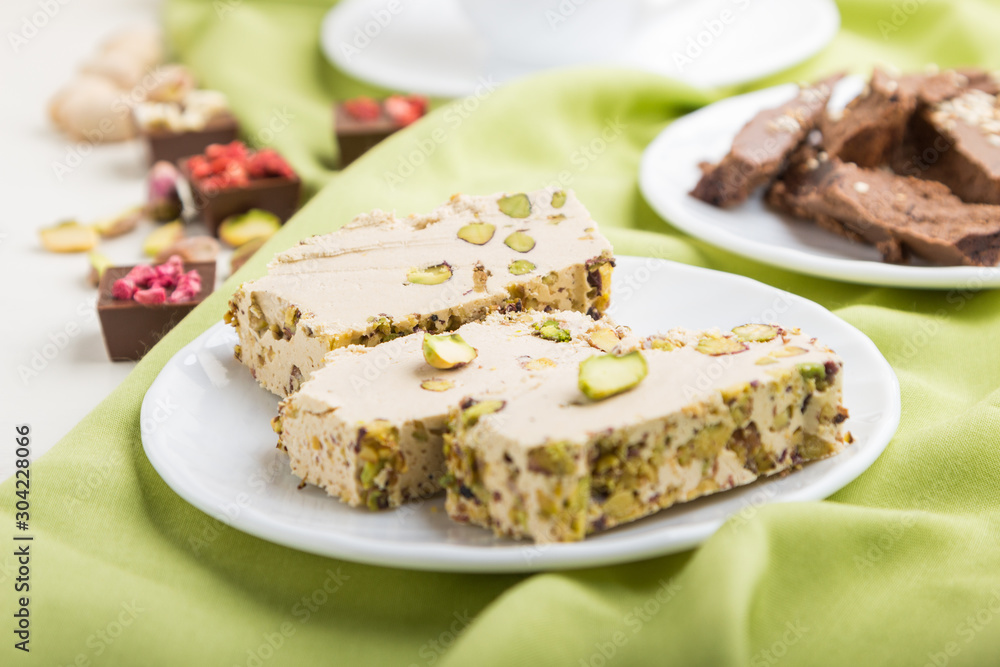 traditional arabic sweets sesame halva with chocolate and pistachio and a cup of coffee on green textile background. side view, selective focus.