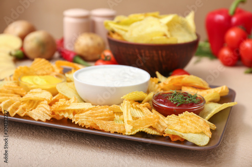 Plate with tasty potato chips, sour cream and tomato sauce on table