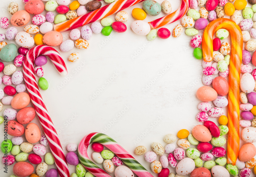 Colorful frame of multicolored candies on a white wooden background. Circle copy space, top view.