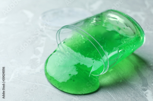 Overturned plastic container with green slime on marble background, closeup