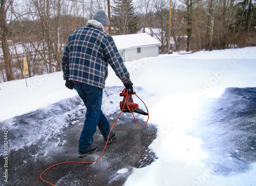 A home owner uses a leaf blower to remove a light powdery snow before it turns to ice on his driveway photo