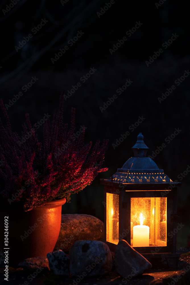 Old lantern with burning candle and ceramic flowerpot, dark night in the garden