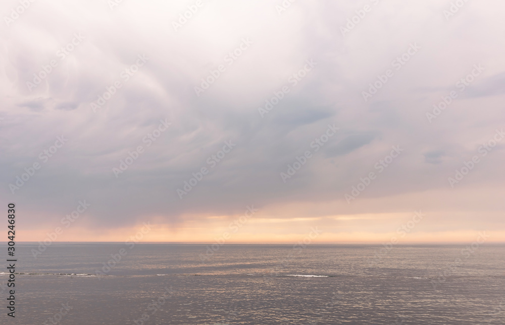 Beautiful dark grey rain clouds colored the shades of pink over the sea at sunset.