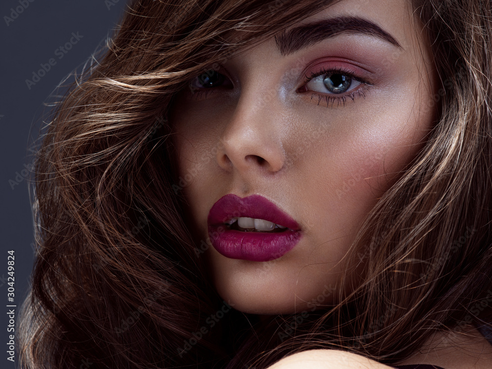 Face of a beautiful woman with long brown curly hair. Fashion model with wavy hairstyle. Attractive young girl with curly hair posing at studio. Female face with purple makeup. Violet make-up. Face of a beautiful woman with long brown curly hair. Fashion model with wavy hairstyle. Attractive young girl with curly hair posing at studio. Female face with purple makeup. Violet make-up.
