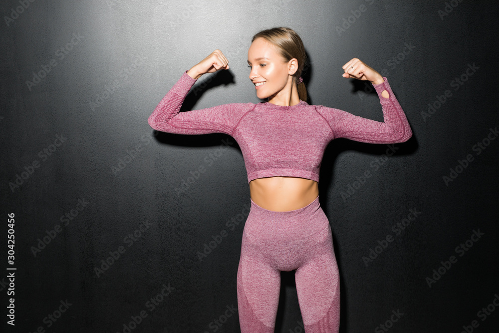 Φωτογραφία Young woman in fitness wear show power isolated on black background