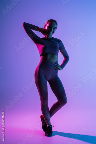 Pretty sporty woman with perfect body standing isolated on purple light background