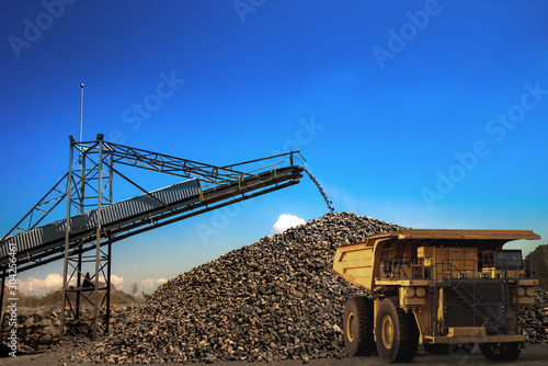Yellow dump truck loading minerals copper, silver, gold, and other at mining quarry.
