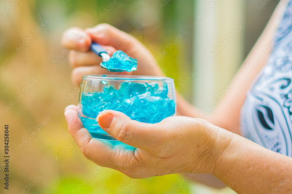 Close of old woman's hands with a jar of desserts in hand eating blue jelly