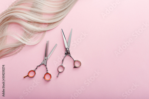 Scissors and other hairdresser's accessories and strand of blonde hair on pink background. Flat lay with space for text. Hairdresser service. Beauty salon service