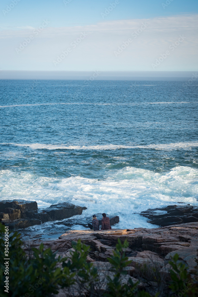 Couple on rocky coast of Maine, admiring the ocean