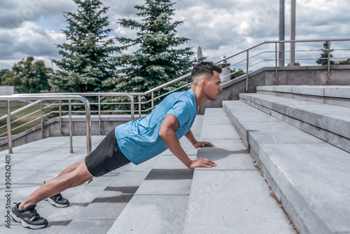 Young sports male athlete, pushing up steps in the summer in the city, workout fitness training, active lifestyle of modern youth, sportswear t-shirt shorts sneakers. Motivation for life.