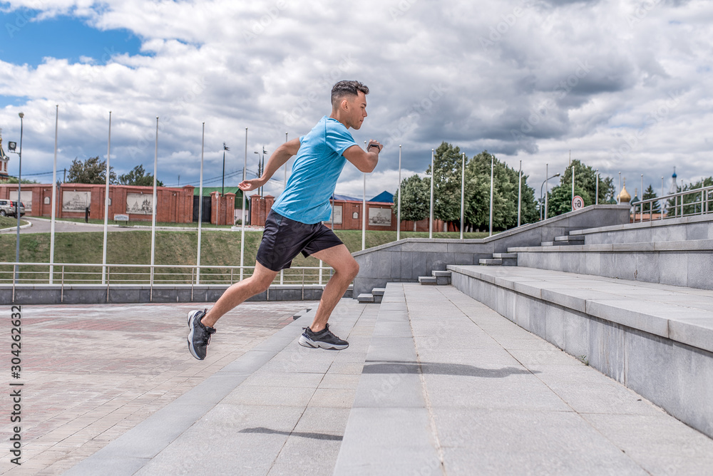 Young sportsman, male athlete, runs up steps, summer day city, workout fitness, active lifestyle of modern youth, sportswear t-shirt shorts sneakers. Motivation for life. Free space and copy text.