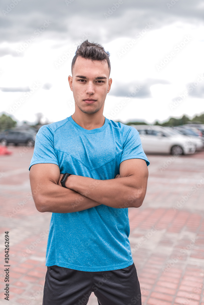 Leader male athlete strong, stands in summer in the city, posing. Fitness workout coach, active lifestyle of modern youth, sportswear t-shirt shorts. Motivation for life. - obrazy, fototapety, plakaty 