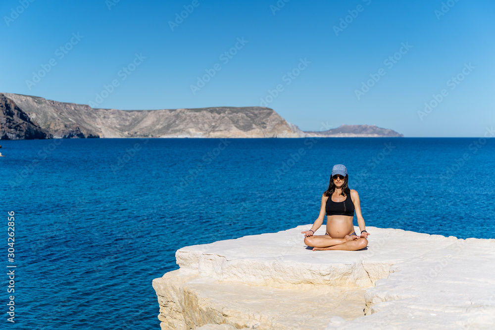 Young pregnant woman practicing yoga next to the mediterranean sea
