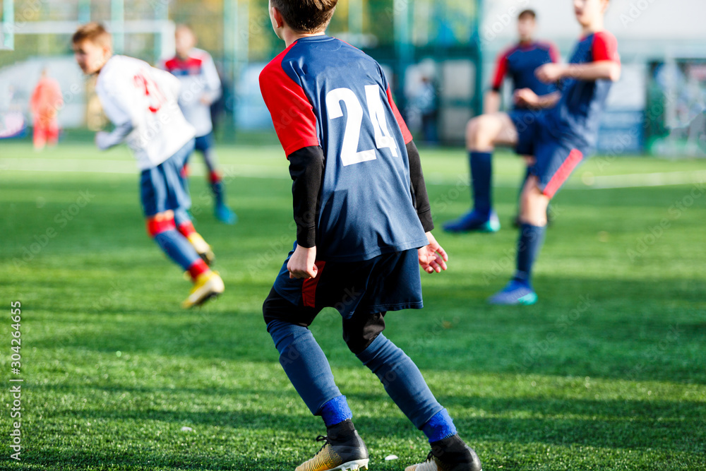 Boys in white and blue sportswear plays football on field, dribbles ball. Young soccer players with ball on green grass. Training, football, active lifestyle for kids concept Boys in white and blue sportswear plays football on field, dribbles ball. Young soccer players with ball on green grass. Training, football, active lifestyle for kids concept