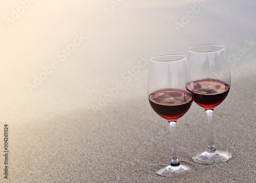 Two wine glasses with red wine on sand on the beach. Valentine's Day concept.
